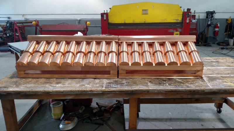 Two custom copper chimney caps on a shop workbench